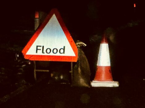 Traffic cones and a flood warning sign are placed on a dark street as a caution for flooding.