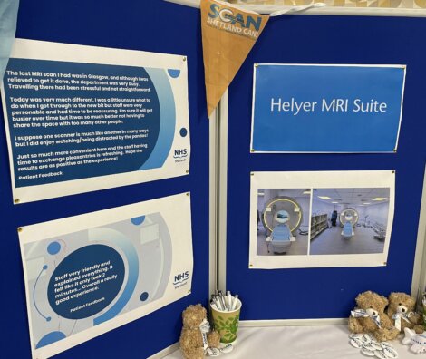 A bulletin board display titled "Helyer MRI Suite" includes printed feedback, photos of MRI machines, and small teddy bears on a table.