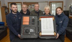 Five people holding an RNLI 200th anniversary display case with tools and a scroll.