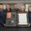 Five people holding an RNLI 200th anniversary display case with tools and a scroll.