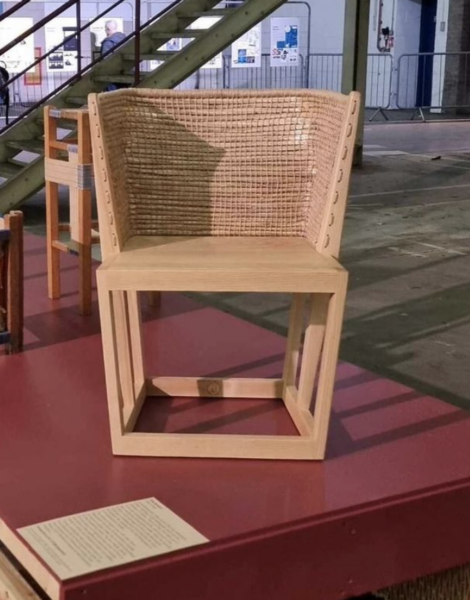 A wooden chair with a woven backrest displayed on a red pedestal inside a building.