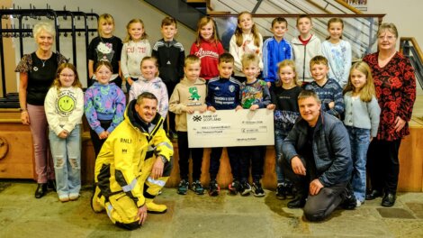 A group of children and adults posing indoors with a large novelty check for the Royal National Lifeboat Institution (RNLI).