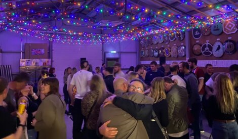 People are gathered at a lively indoor party with colorful string lights above.