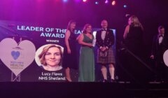 Group of people on stage at an award ceremony, with a screen displaying "Leader of the Year Award" and "Lucy Flaws, NHS Shetland.