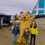 Three children pose with a person in a bear costume in front of a small airplane on an overcast day.