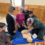 A group of people participates in a CPR training session, observing as an instructor demonstrates on a mannequin.