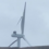 A damaged wind turbine with broken blades stands against a cloudy sky.