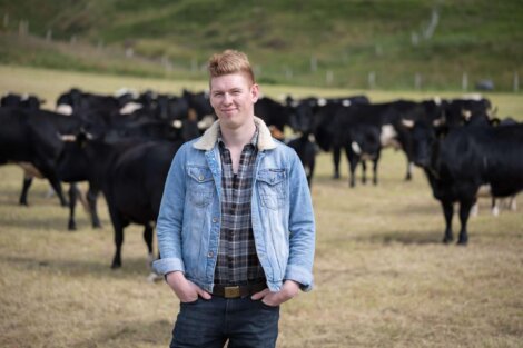 A person standing in a field with a herd of cows in the background.