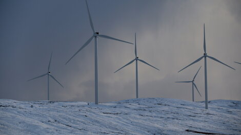 Wind turbines on a snow-covered hill under a cloudy sky.