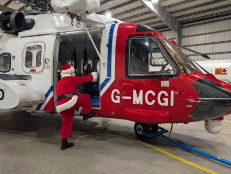 Santa Claus climbing into a red and white helicopter in a hangar.