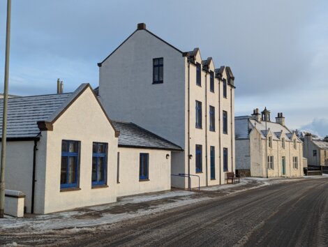 White buildings with blue-trimmed windows line a snow-dusted street under a cloudy sky.