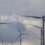 Wind turbines under a cloudy sky, blades spinning gently in a field.