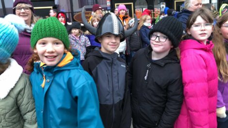 Group of children dressed in winter clothing stand together; one wears a Viking helmet.