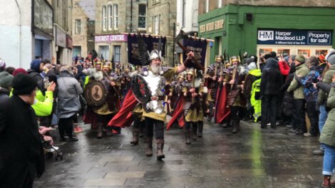 Parade with people in Viking costumes marching through a town street, surrounded by onlookers.