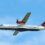 Twin-engine Loganair airplane with a red and black tartan tail livery flying against a blue sky.