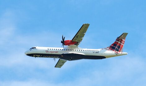 Twin-engine Loganair airplane with a red and black tartan tail livery flying against a blue sky.