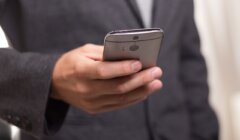 A person in a suit holds a smartphone in one hand.