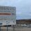 Sign for Staneyhill Development Infrastructure Contract with contractor details in foreground; construction site and machinery visible in the background under a cloudy sky.