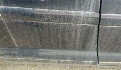 A close-up of a black car door covered in dust and dirt, showing streaks and grime buildup on the surface.