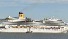 A large white cruise ship with multiple decks moves through the water accompanied by a small tugboat.