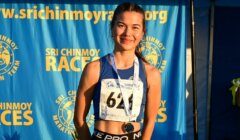 A young female runner wearing bib number 643 stands smiling in front of a Sri Chinmoy Races backdrop, with a medal around her neck.