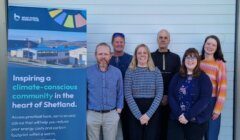 Six people stand smiling beside a banner for the Brae Rural Energy Hub, which promotes climate-conscious community action in Shetland.