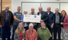 Ten people pose indoors, holding a large cheque for £400 from the Bank of Scotland with "Viking Genes Fund" written on it. Three people are kneeling in front, and seven are standing behind.