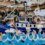 People dressed in sailor and pirate costumes sit on a parade float shaped like a ship, holding buckets and water guns, with decorations of waves and seagulls.