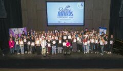 A large group of people on stage hold certificates at the Saltire Awards Ceremony 2025, with a presentation screen and banners in the background.