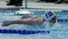 Swimmer in a cap and goggles performing the butterfly stroke in a swimming pool during a competition.