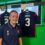 A young athlete wearing a navy polo shirt with the number 3 stands beside a Scotland football jersey labeled "SMITH 3" hanging on display.