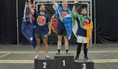 Three male athletes stand on a podium holding trophies and country flags. The podium is labeled 1, 2, and 3, with a backdrop featuring event branding.