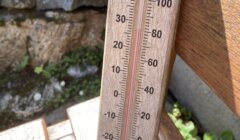 A wooden thermometer shows a temperature of approximately 32°C (90°F) outdoors, with a stone wall and greenery in the background.