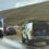 An ambulance and police vehicle are parked on the side of a rural road with flashing lights on, near two other cars.
