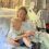 A woman in a hospital bed holds a young child on her lap. The child is playing with a medical device attached to the woman's hand.