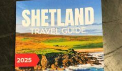 Cover of the "Shetland Travel Guide 2025" featuring a coastal landscape with green hills and blue sea under a clear sky.