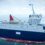 A modern, medium-sized research vessel with a blue hull and white superstructure sails on calm water under a cloudy sky.