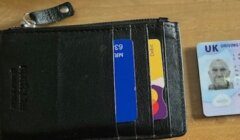 A black leather wallet with bank cards partially visible, next to a UK driving licence on a wooden surface.