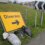 A yellow "Diversion" road sign with a right arrow is propped up on grass with sandbags, next to a road curve sign by a roadside fence.