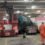 A truck tilted and crashed onto a car and van in a parking garage, while three workers in safety gear observe the scene.