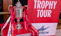 A silver trophy with red and white ribbons labeled "Scottish Gas" is displayed next to a sign reading "Trophy Tour Presented by NorthLink Ferries.