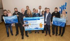 A group of people stands indoors holding a large "Fishing For Litter" banner, celebrating 20 years and 23,000 tonnes of marine litter removed from Scottish seas.