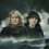 Two women stand in front of stormy ocean waves under a dark, cloudy sky.