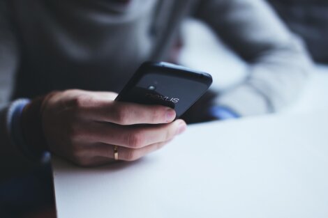 A person wearing a grey long-sleeve shirt and a gold ring holds a black Nexus smartphone while sitting at a white table.