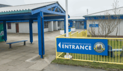 The main entrance of Sandwick Junior High School, with a blue sign and yellow railings in front of the building.