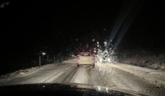 A car is stopped on a snowy, wet road at night, with headlights from an oncoming vehicle visible in the background.