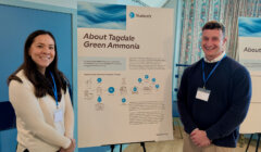 Two people stand smiling next to a presentation board titled "About Tagedale Green Ammonia" at what appears to be an informational event.