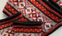 A knitted scarf and fingerless gloves with a red, black, white, and yellow geometric pattern are laid out on a light surface.