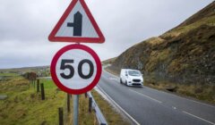 A speed limit sign showing 50 and a junction warning sign beside a rural road with a white van driving past.