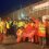 A group of workers in high-visibility clothing stand outside Sullom Voe Terminal at night, holding union flags and raising their fists.